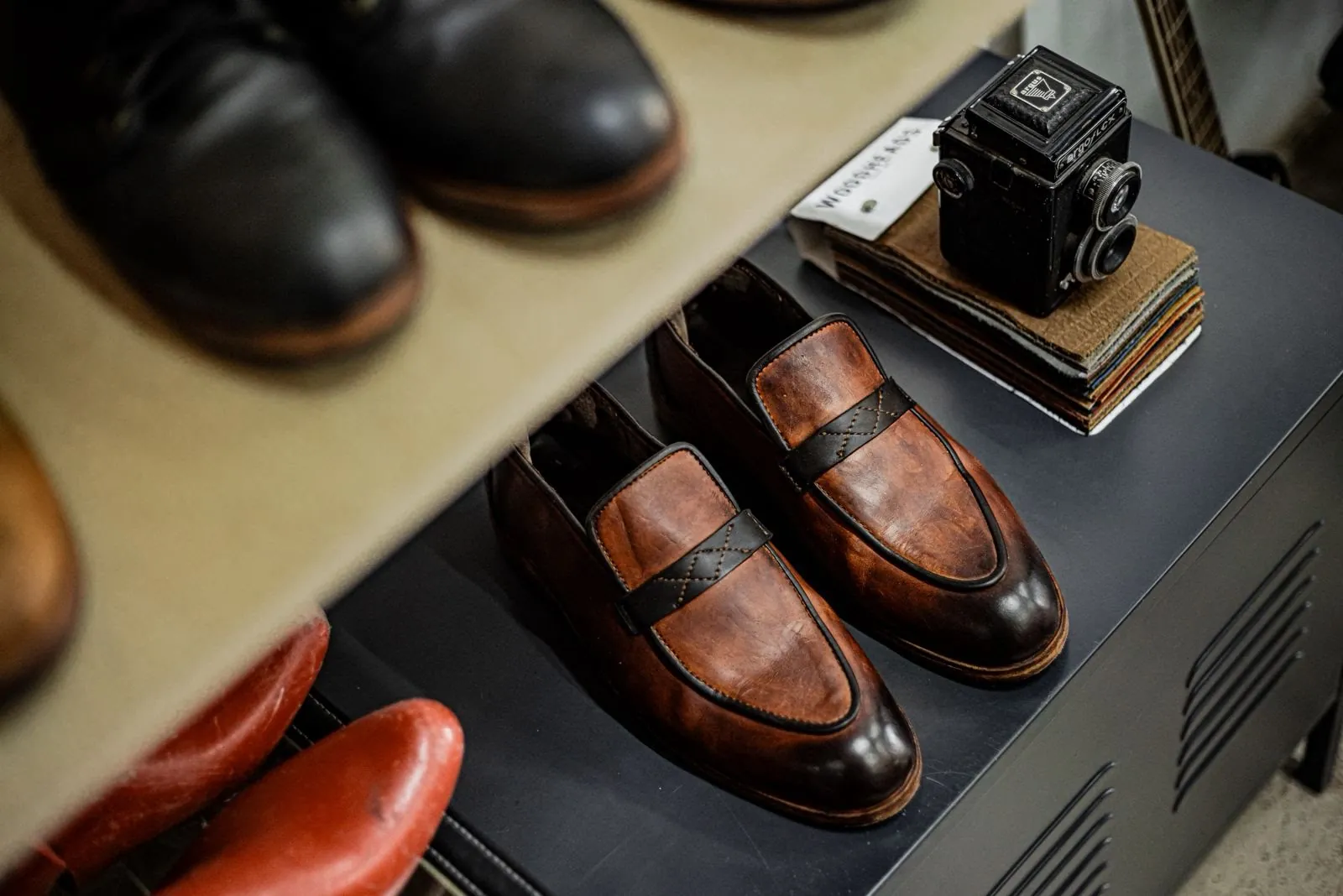 A pair of brown loafers on a shelf in the Room, beside an old camera