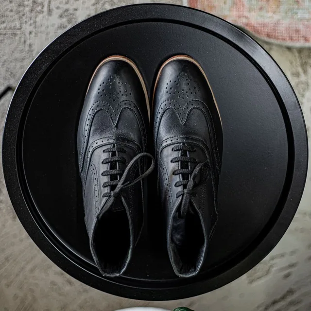 Black brogue shoes on a round black table, seen from above