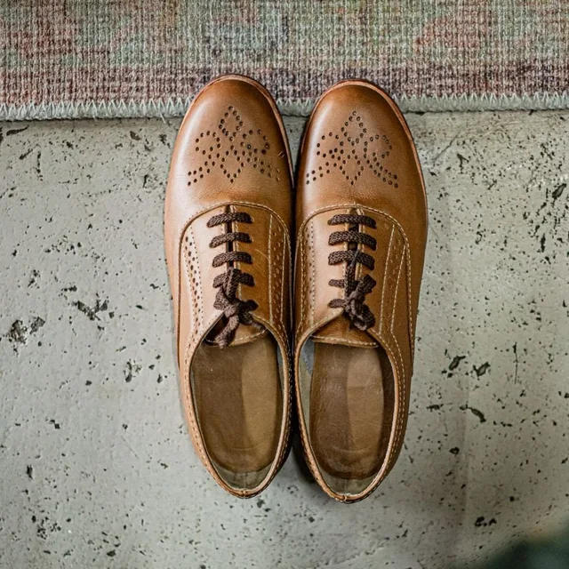 A pair of tan brogue shoes on a stone floor, seen from above