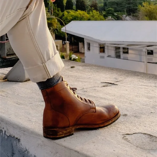 A tan lace-up boot, worn, on a low wall outdoors